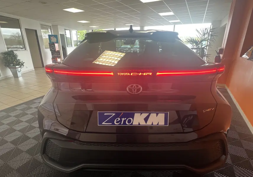 Vue arrière du Toyota C-HR 1.8 Hybrid 2024 en améthyste métal avec feux LED horizontaux allumés en intérieur showroom.