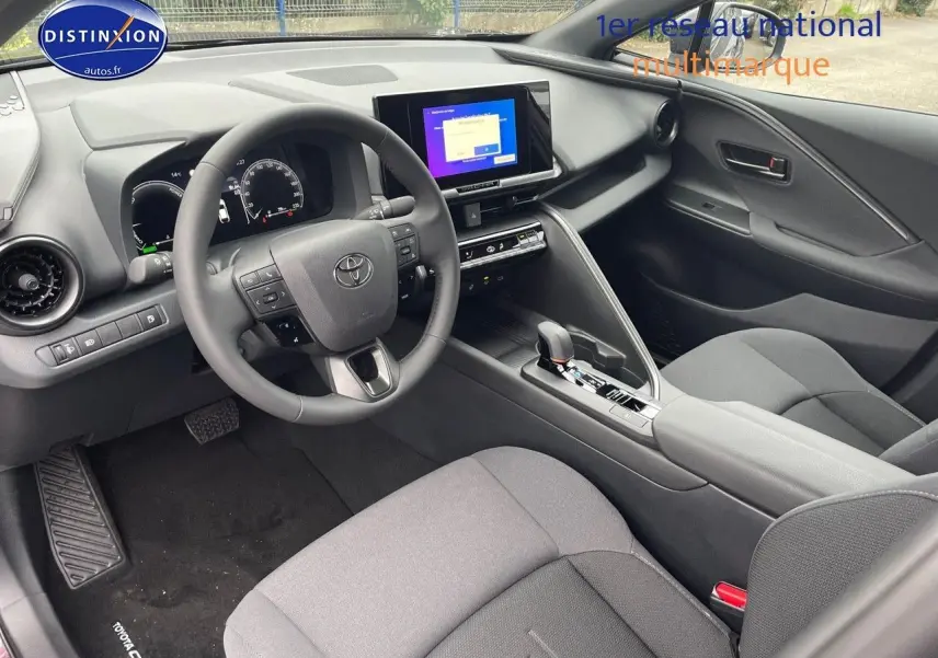 Vue intérieure côté conducteur du Toyota C-HR 1.8 Hybrid 2024 avec tableau de bord moderne et sièges gris foncé.