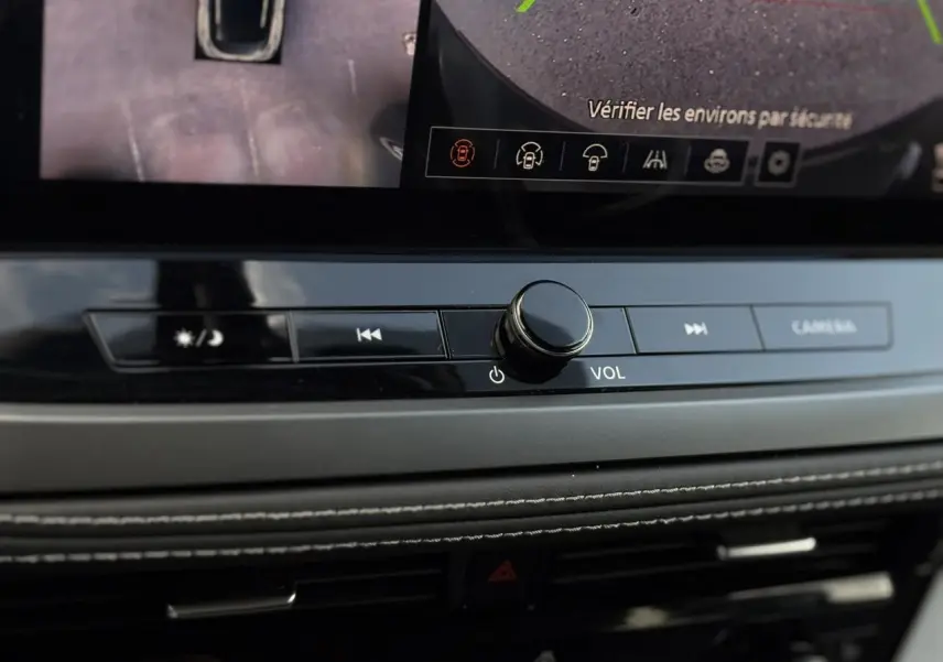 Gros plan sur la console centrale du Nissan Qashqai 2025, boutons de volume et caméra avec écran tactile visible.
