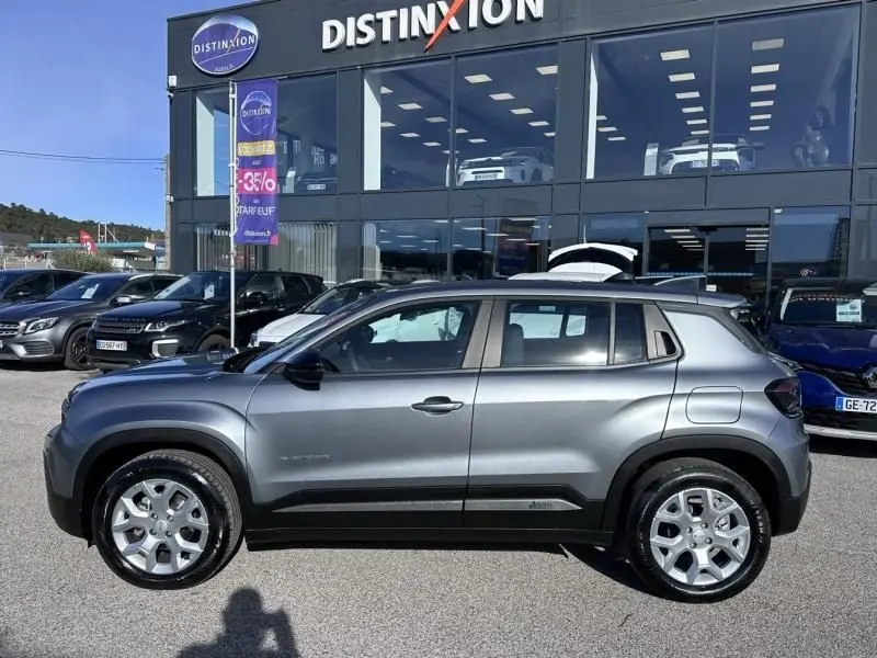 Vue de profil côté gauche d'un Jeep Avenger gris métallisé 2025 garé devant un concessionnaire Distinxion.