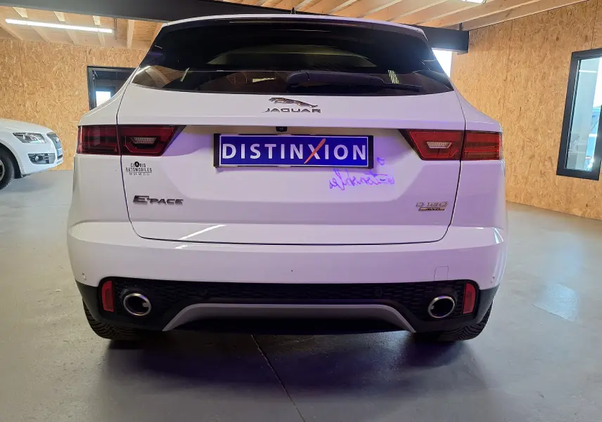 Vue arrière du Jaguar E-PACE blanc 2019 avec double sortie d'échappement et feux arrière LED dans un garage.