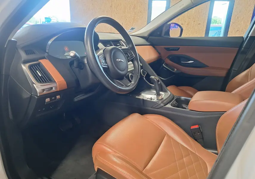 Intérieur côté conducteur du Jaguar E-PACE blanc 2019, sièges cuir marron et tableau de bord moderne.
