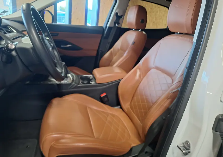 Intérieur Jaguar E-PACE blanc vu côté gauche, sièges avant en cuir marron avec surpiqûres losanges.