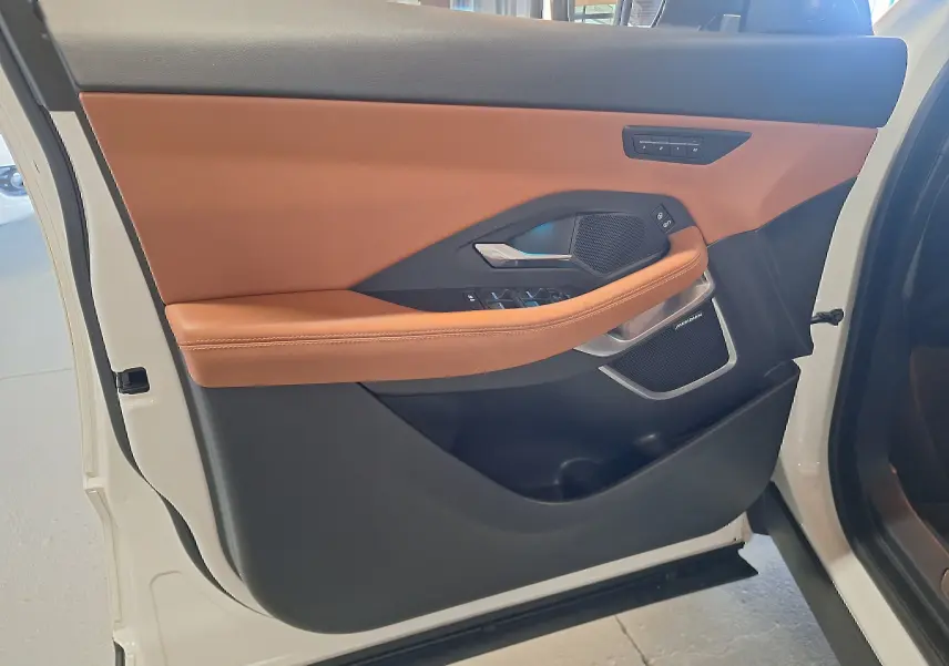 Gros plan sur la porte avant gauche blanche d'un Jaguar E-PACE 2019 avec garniture cuir marron et haut-parleur Meridian.