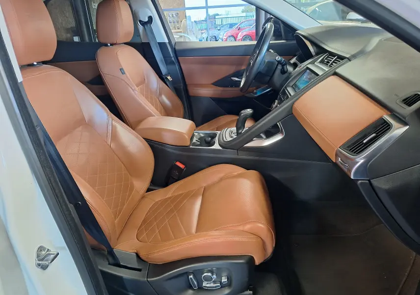 Intérieur côté conducteur du Jaguar E-PACE blanc 2019 avec sièges cuir marron et tableau de bord assorti.