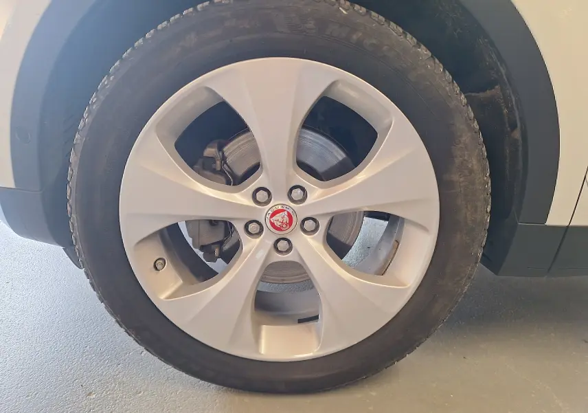 Gros plan sur la roue avant droite du Jaguar E-PACE blanc, mettant en valeur la jante argentée et le logo central rouge.