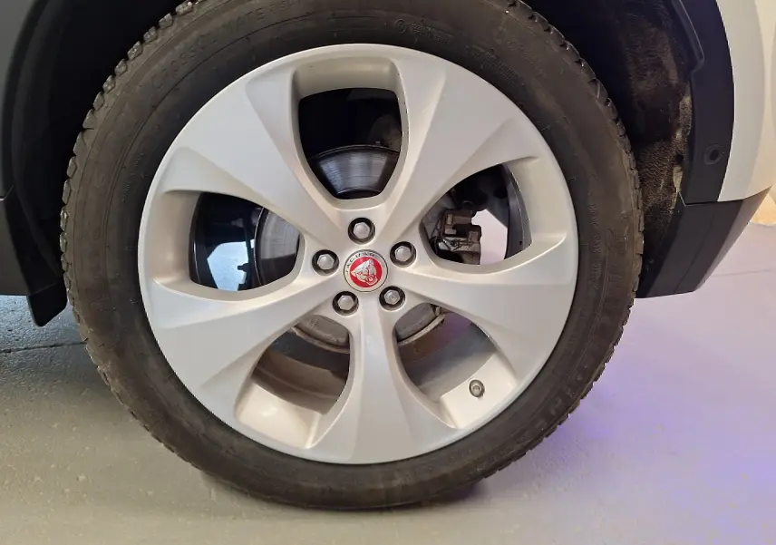 Gros plan sur la roue avant droite du Jaguar E-PACE blanc 2019 avec jante alliage et logo Jaguar central rouge.