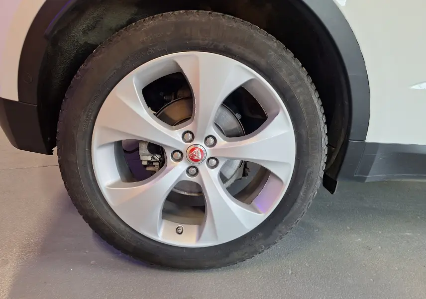 Gros plan sur la roue avant droite d'un Jaguar E-PACE blanc avec jante argentée et logo Jaguar rouge au centre.