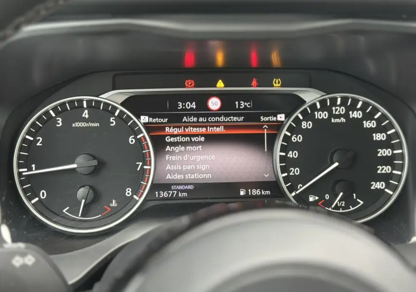 Tableau de bord du Nissan Qashqai 2024 avec compte-tours, vitesse, et écran d'aide au conducteur affichant les alertes.
