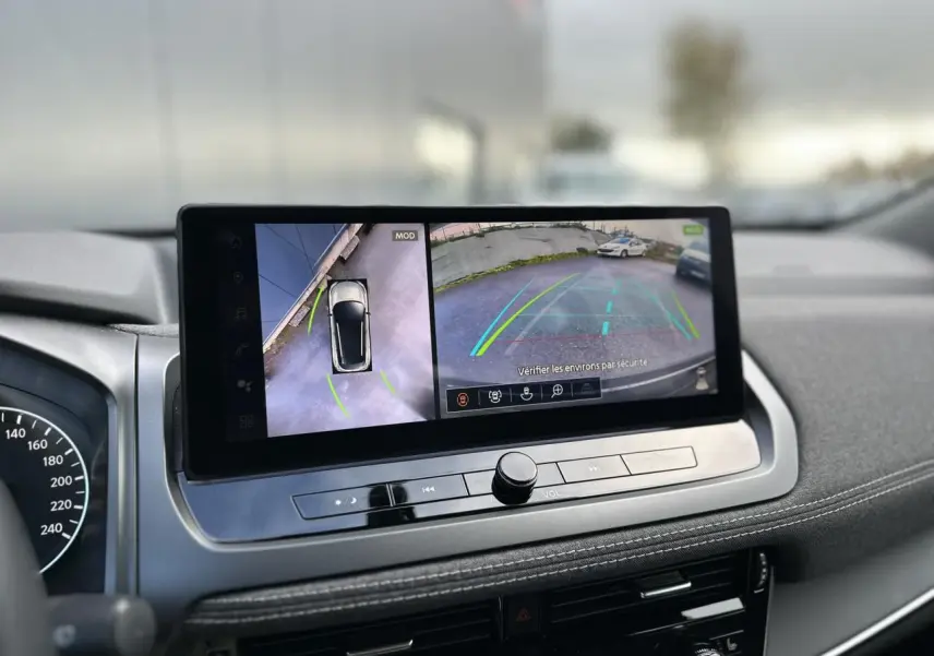 Vue intérieure du tableau de bord du Nissan Qashqai 2024 avec écran tactile affichant la caméra de recul et vue 360° du véhicule.