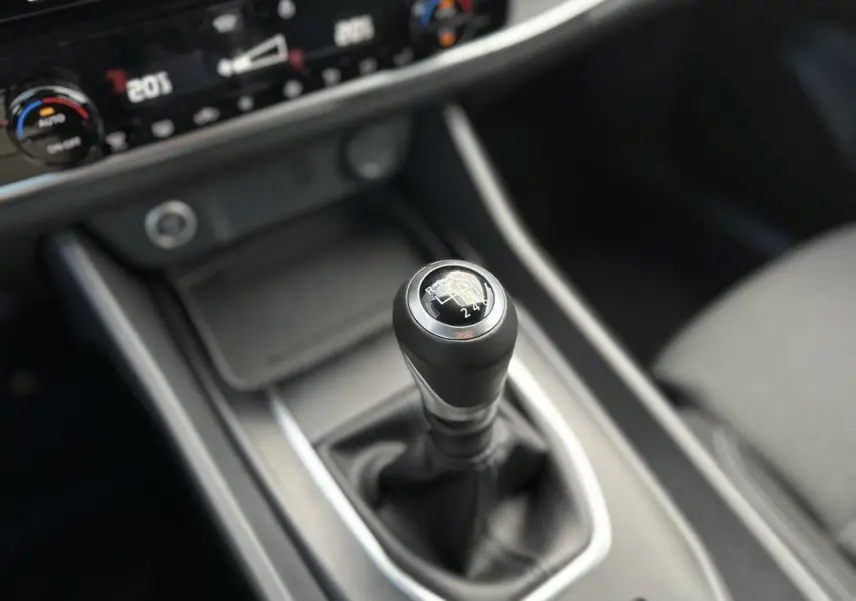 Gros plan sur le levier de vitesses manuel noir du Nissan Qashqai 2024 avec console centrale et commandes climatisation visibles.