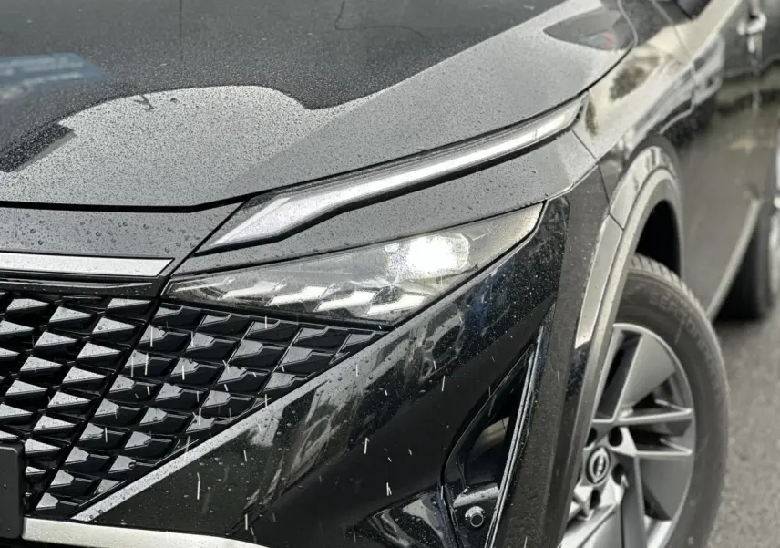 Gros plan sur l'avant droit noir nacré du Nissan Qashqai 2024, mettant en valeur son phare LED et la calandre texturée.