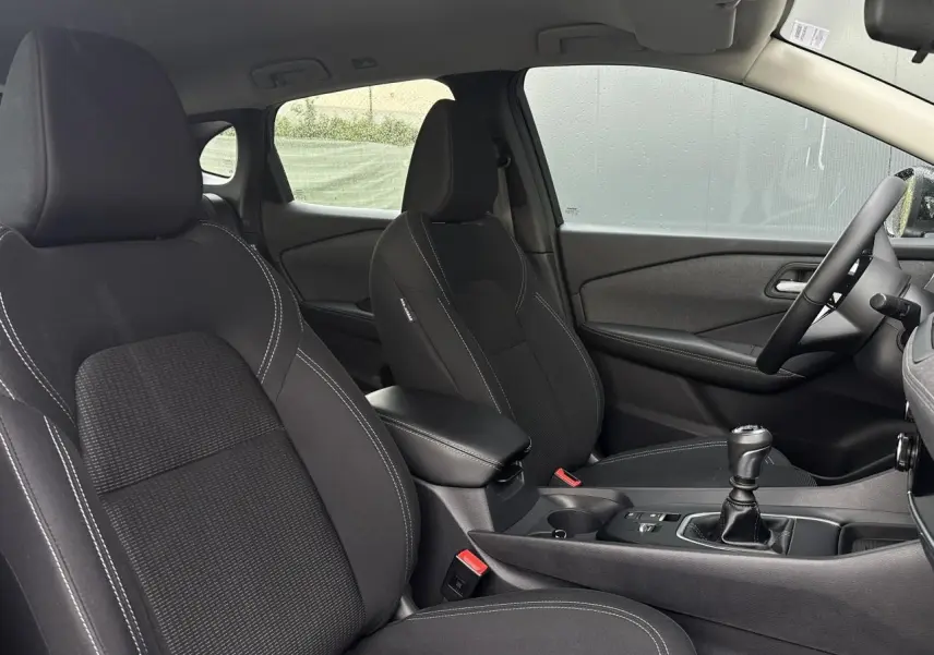 Vue intérieure côté droit du Nissan Qashqai 2024 noir nacré, sièges avant noirs avec coutures blanches et levier de vitesse manuel.