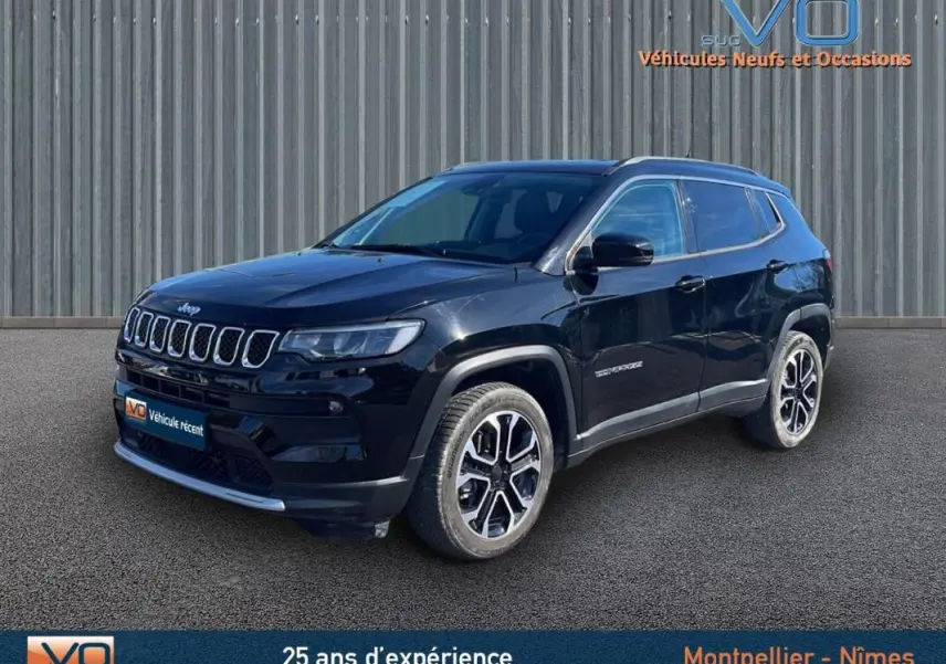 Jeep Compass noir en 3/4 avant droit, avec barres de toit et jantes 18 pouces visibles sur fond industriel.