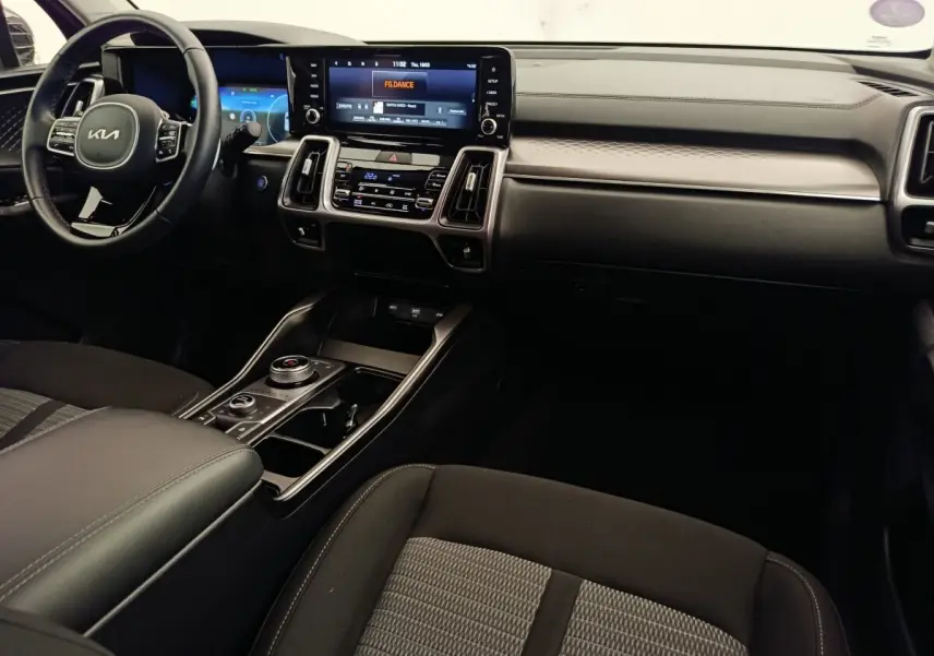 Vue intérieure du tableau de bord et console centrale du Kia Sorento 2023 hybride, avec écran tactile et volant cuir noir.