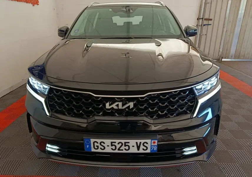 Vue frontale d’un KIA Sorento noir 2023 avec calandre noire et feux LED allumés dans un garage.