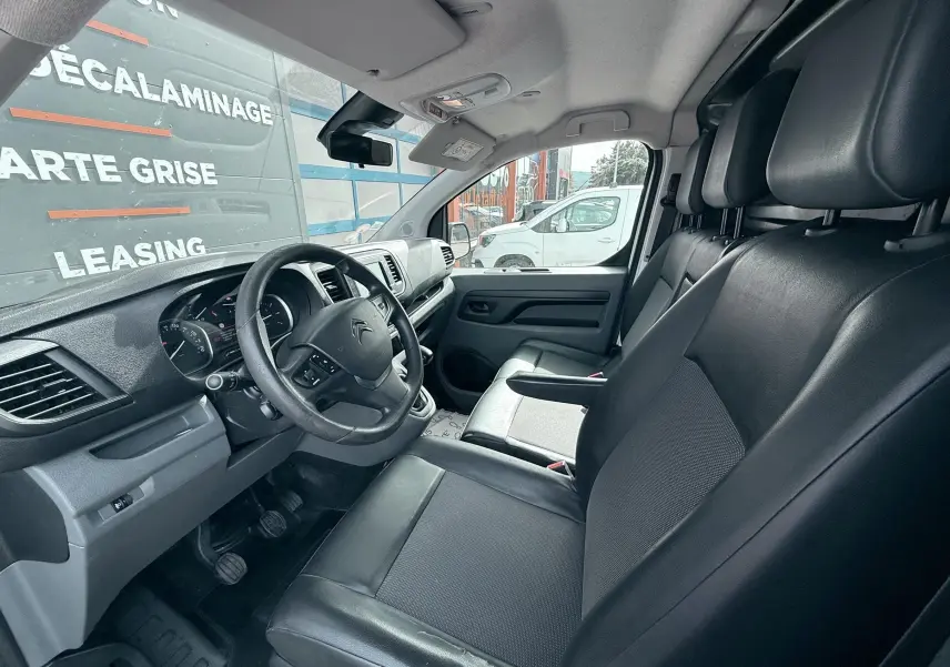 Vue intérieure côté conducteur du Citroën Jumpy blanc de 2017, montrant les sièges noirs en cuir et le tableau de bord.