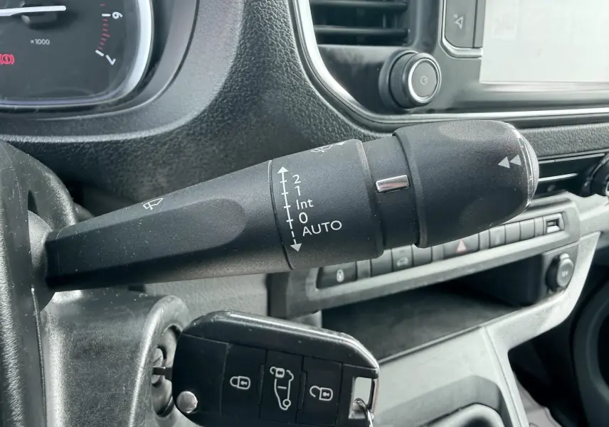 Gros plan sur la commande d’essuie-glace noire et la clé insérée dans le contact d’un Citroën Jumpy blanc, intérieur gris.