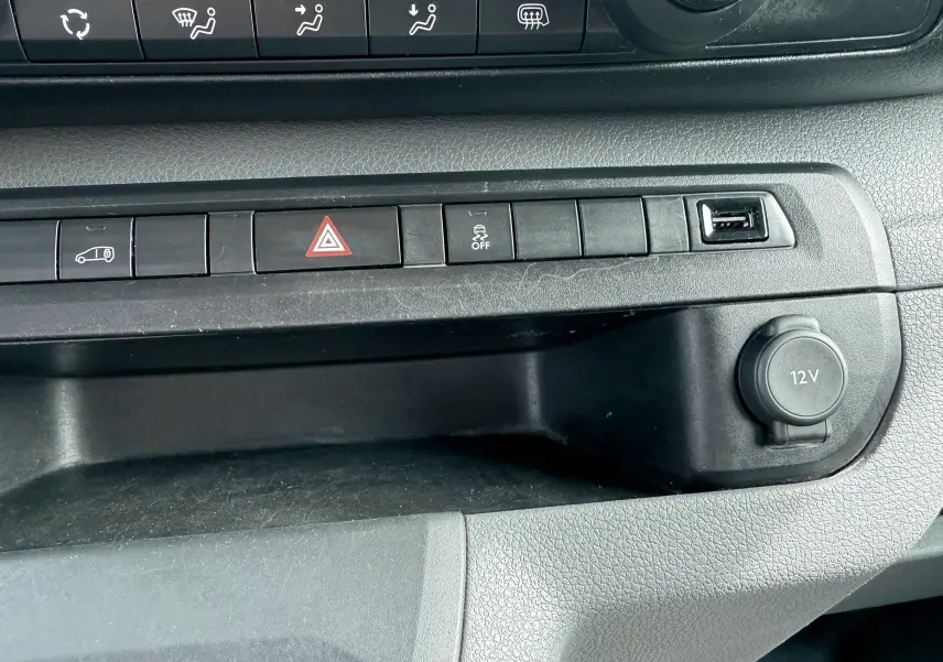 Vue rapprochée de la console centrale noire du Citroën Jumpy blanc, avec boutons de commande et prise 12V visible.