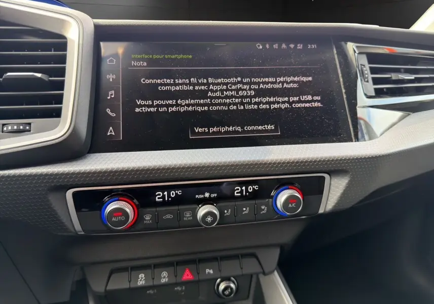 Vue rapprochée du tableau de bord de l'Audi A1 Sportback blanc 2025, mettant en valeur l'écran tactile et la climatisation bizone.