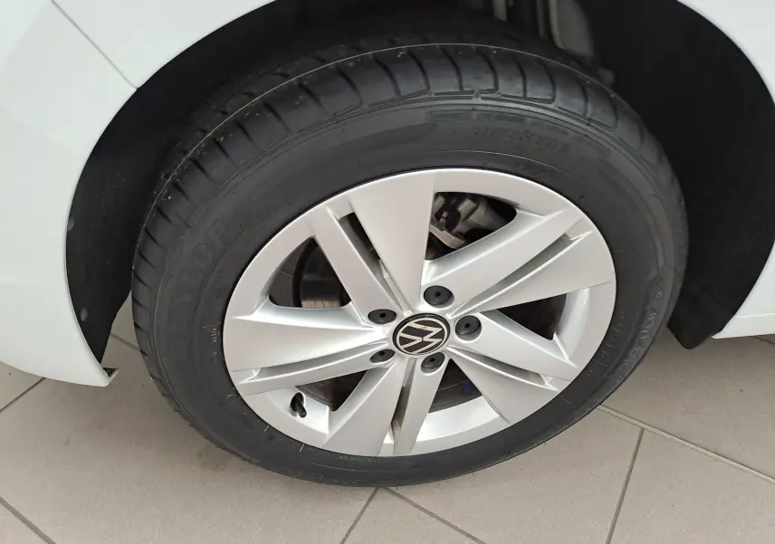 Gros plan sur la roue avant gauche d'une Volkswagen Golf blanche avec jante alliage et logo VW central.