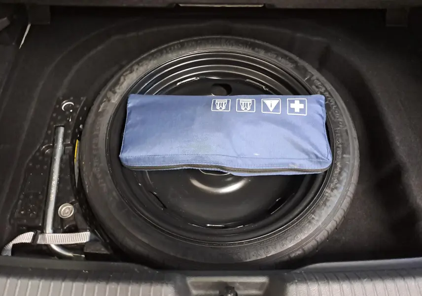 Vue plongeante sur la roue de secours noire et la trousse de secours bleue dans le coffre d'une Volkswagen Golf blanche 2022