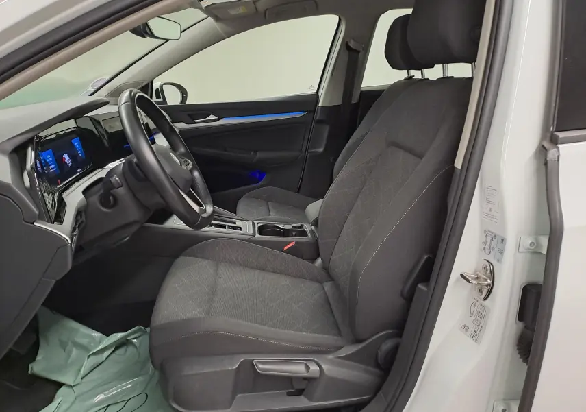 Intérieur côté conducteur d'une Volkswagen Golf blanc pur 2022, sièges gris et tableau de bord digital avec éclairage bleu.