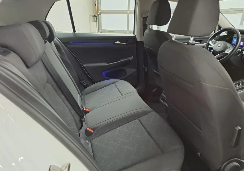 Intérieur arrière de la Volkswagen Golf blanc pur 2022, vue côté gauche avec sièges tissu et éclairage d'ambiance bleu.
