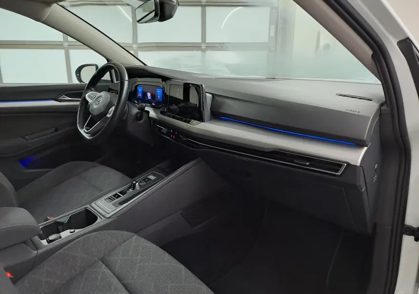 Intérieur avant droit de la Volkswagen Golf 1.5 TSI blanche, avec tableau de bord moderne et éclairage d'ambiance bleu.