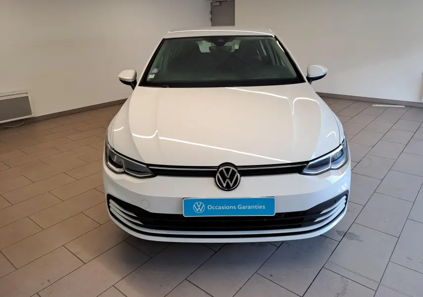 Vue avant d'une Volkswagen Golf blanche Pure de 2022 avec calandre noire et plaque "Occasions Garantis" en intérieur showroom.