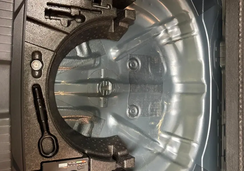 Coffre ouvert du Volkswagen T-Roc 2024 bleu pétrole, montrant le rangement pour roue de secours et outils intégrés.