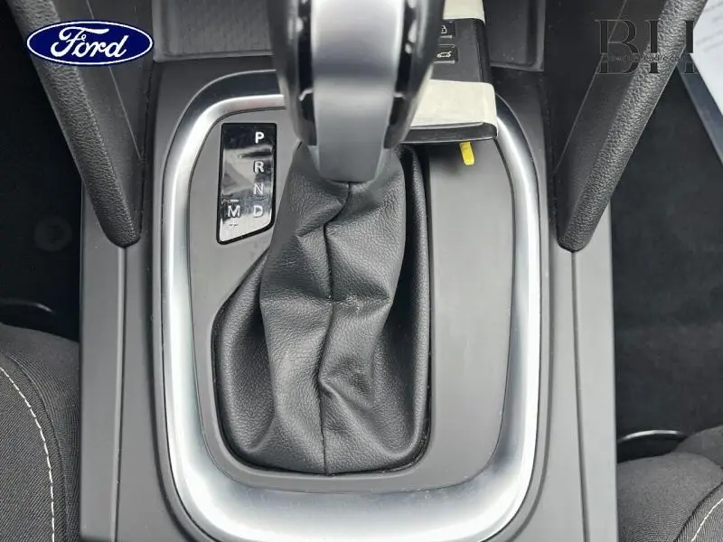 Gros plan sur la console centrale avec levier de boîte automatique noir et garniture grise, intérieur sombre.