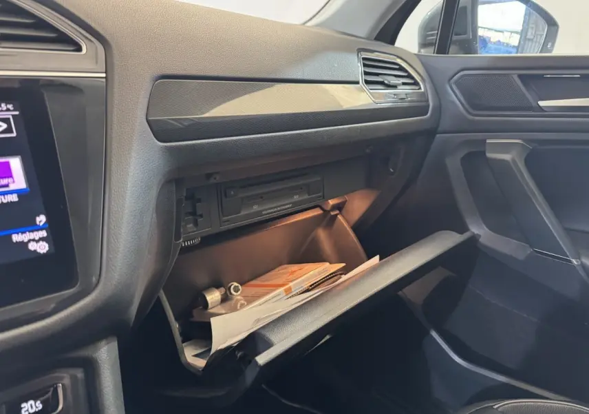 Intérieur côté passager du Volkswagen Tiguan Allspace gris, boîte à gants ouverte avec documents visibles.