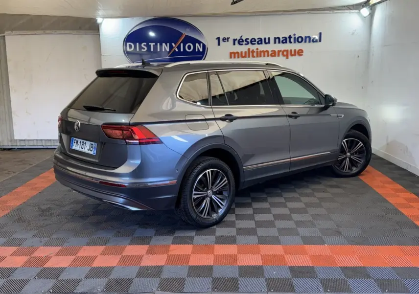 Vue 3/4 arrière droite d’un Volkswagen Tiguan Allspace gris foncé avec jantes alliage et vitres teintées en intérieur showroom.