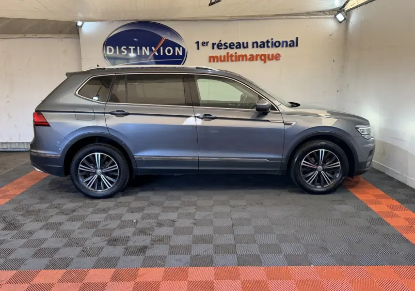 Volkswagen Tiguan Allspace gris foncé vu de profil côté gauche dans un showroom avec jantes alliage noires.
