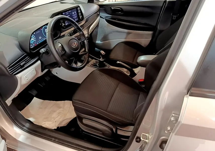 Vue intérieure côté conducteur de la Hyundai i20 gris clair 2022, volant cuir multifonctions et tableau de bord digital.