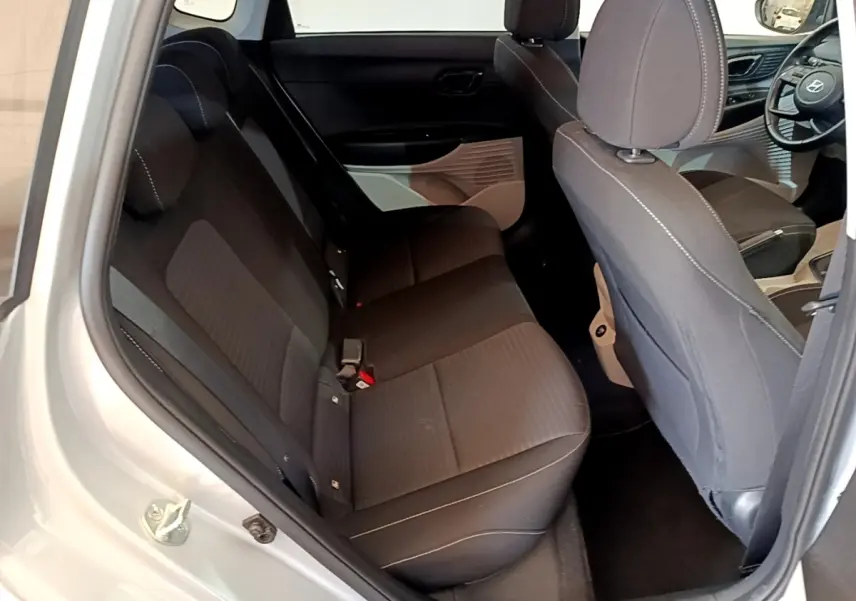 Vue intérieure côté gauche montrant les sièges arrière noirs et partie avant avec volant cuir d'une Hyundai i20 gris clair 2022.