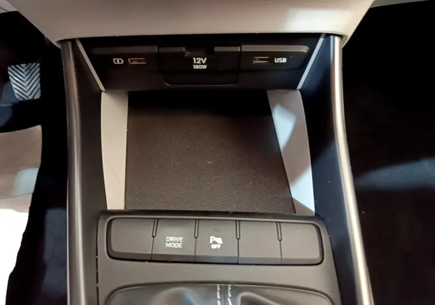 Gros plan sur la console centrale noire du Hyundai i20 2022, montrant prises USB, prise 12V et boutons de contrôle.