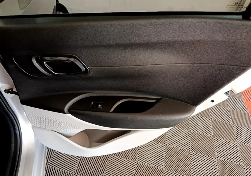 Vue intérieure du panneau de porte avant gauche gris clair de la Hyundai i20 2022 avec poignée et commande de fenêtre.