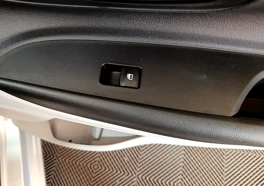 Gros plan sur le bouton de verrouillage des portes dans la portière intérieure noire d'une Hyundai i20 gris clair.