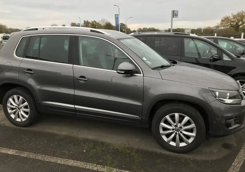 Vue de profil côté gauche d'un Volkswagen Tiguan Sportline gris foncé, avec jantes alliage et toit ouvrant visible.