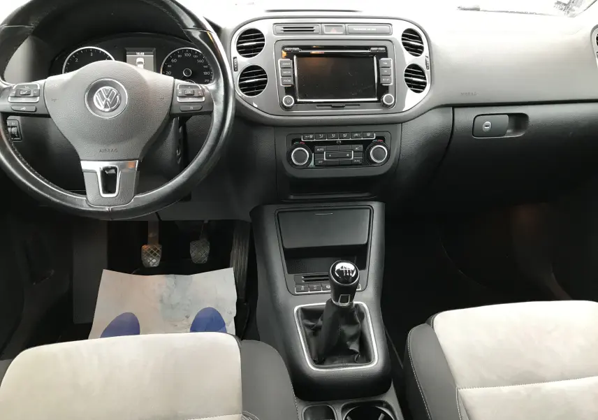 Vue intérieure avant du Volkswagen Tiguan Sportline 2012, tableau de bord noir avec volant multifonction et levier de vitesse manuel.