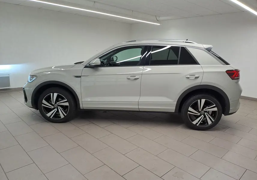 Vue de profil côté gauche du Volkswagen T-Roc 1.5 TSI R-Line 2024 en gris Ascot avec jantes alliage distinctives.