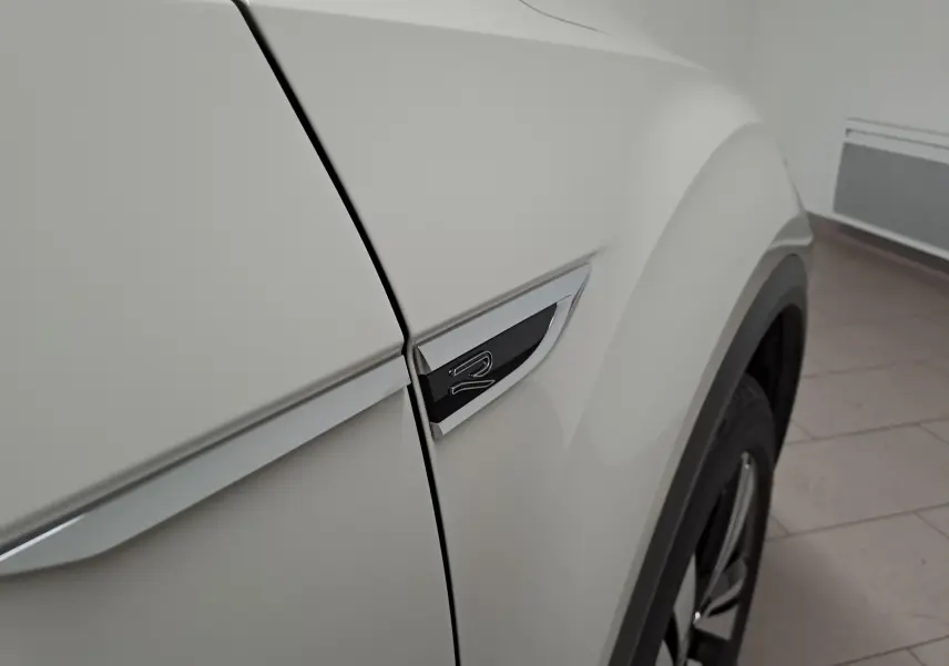 Gros plan sur l'aile avant droite gris Ascot du Volkswagen T-Roc 2024 avec logo R-Line et jante visible.