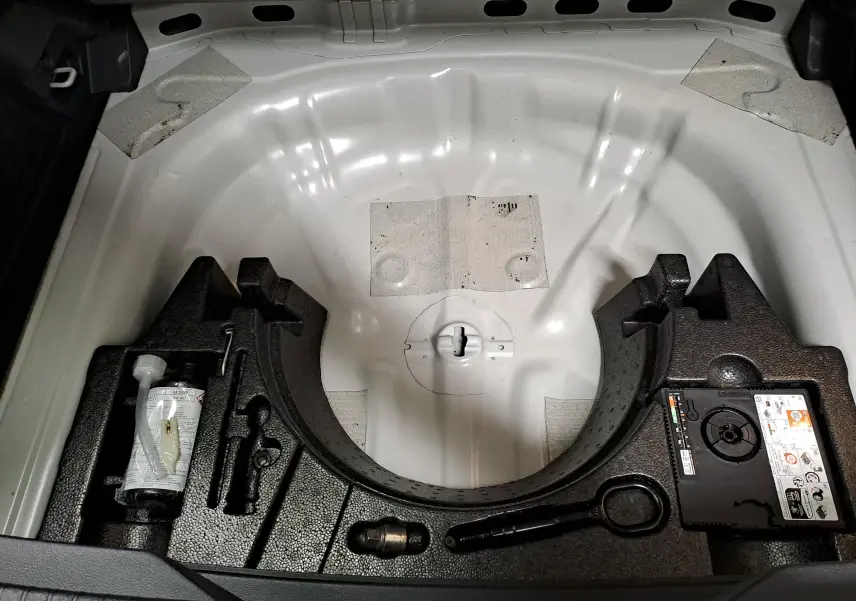 Vue plongeante sur le compartiment de roue de secours vide du Volkswagen T-ROC gris Ascot, avec outils et compresseur intégrés.