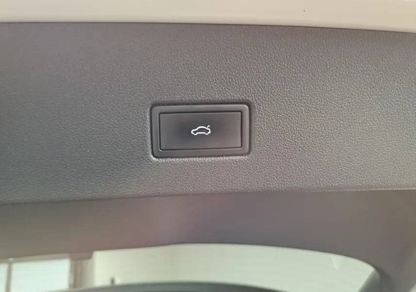 Bouton d'ouverture électrique du coffre sur la garniture intérieure du hayon d'un Volkswagen T-Roc gris Ascot 2024.