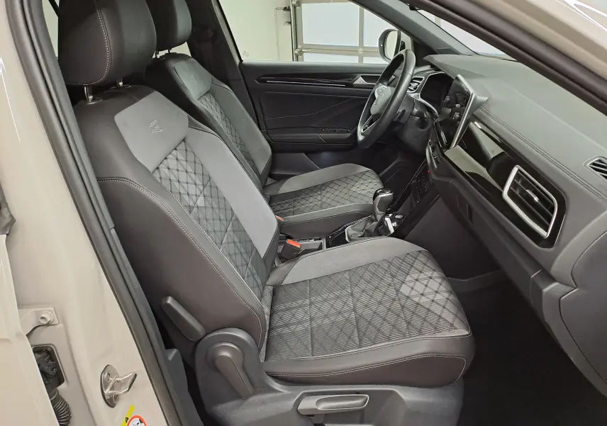 Intérieur du Volkswagen T-Roc 2024 vu côté conducteur, sièges gris à motif losanges et tableau de bord moderne noir.