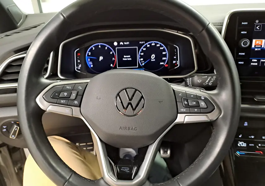 Vue rapprochée du volant multifonction noir du Volkswagen T-Roc 2024 R-Line avec tableau de bord numérique allumé.