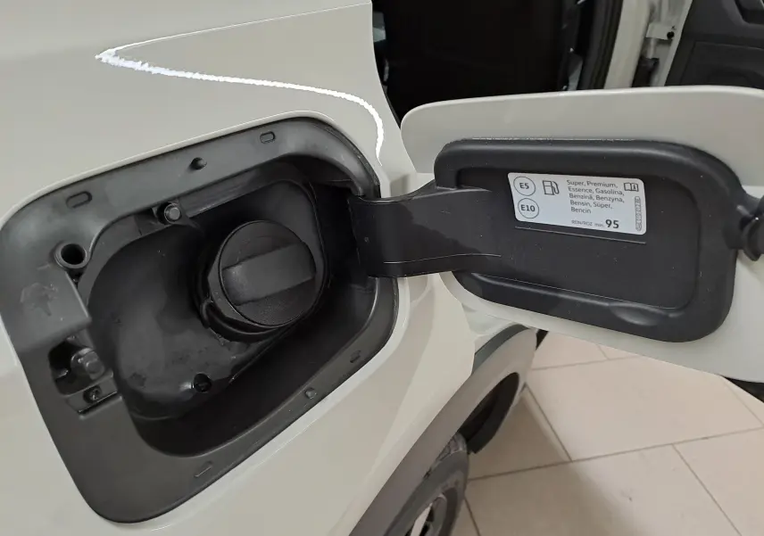 Gros plan sur la trappe à carburant ouverte du Volkswagen T-Roc Gris Ascot, montrant le bouchon essence et l'étiquette de carburant.