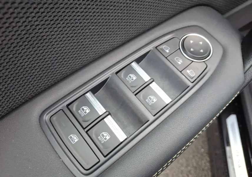 Gros plan sur les commandes de lève-vitres et rétroviseurs sur la porte côté conducteur d’une Renault Symbioz noire.